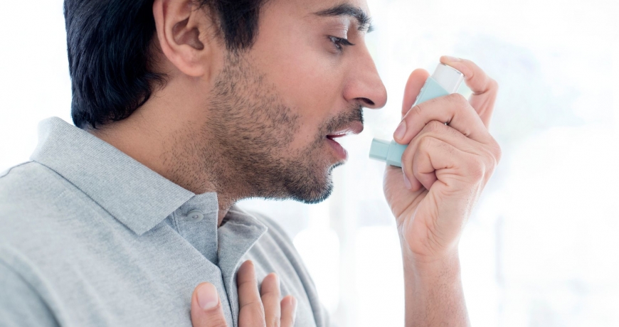 Astma często wymaga użycia inhalatora. Na zdjęciu mężczyzna korzysta z niego, bo odczuwa wyraźne duszności.