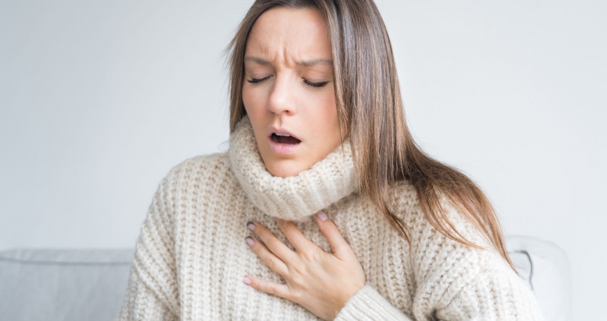 Kobieta w swetrze odczuwa ciężki oddech w klatce piersiowej.