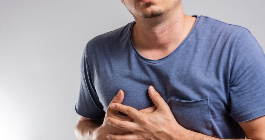 Mężczyzna w niebieskiej koszulce chwyta się za klatkę piersiową. Możliwe, że występuje u niego niewydolność płucna.