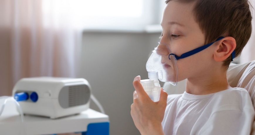Chłopiec, którego dotknęła przewlekłą obturacyjna choroba płuc POChP, wspomaga oddech inhalatorem.